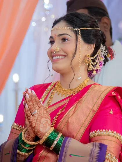 A moment of prayer and gratitude. This image captures the bride's traditional accessories, including the 'mundavalya' (forehead ornament), against her glowing makeup and happy smile.