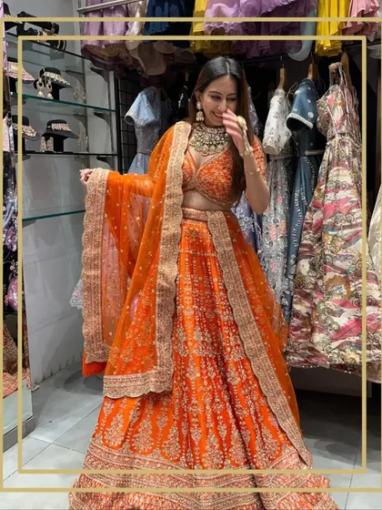 A client having fun trying on a vibrant orange lehenga in my store. The joy of dress-up is for everyone.