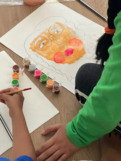 Two children working side-by-side on their self-portraits, each with their own distinct style and approach.