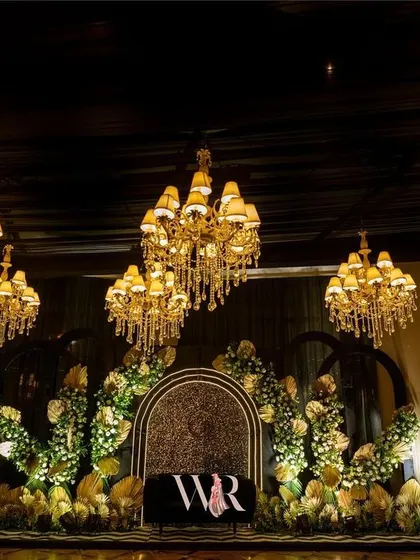 The stage area under dramatic lighting, with chandeliers hanging above. The design combines floral elements with modern, clean lines for a sophisticated look.