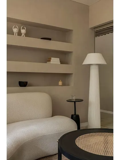 The client lounge is designed as a peaceful retreat, featuring a custom-designed curved sofa in a textured white fabric. Built-in wall niches provide space for subtle decor, while a tall, fluted floor lamp casts a soft, ambient glow.