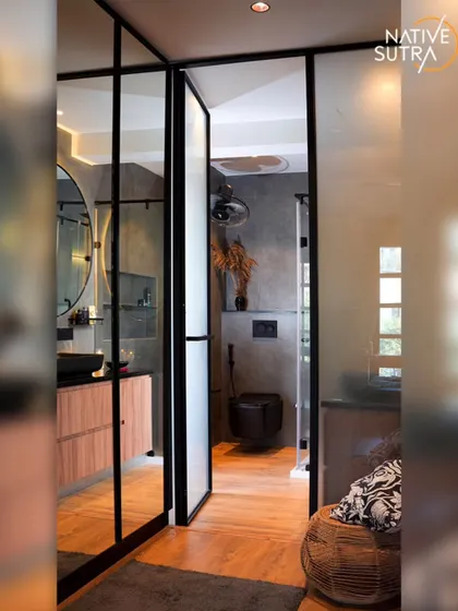 This industrial-chic bathroom features a large, round backlit mirror and a black vessel sink. The design uses dark tones, raw materials, and glass partitions to create a sophisticated and masculine sanctuary.