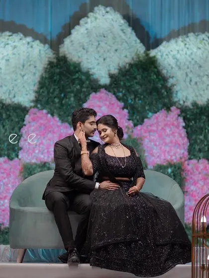 A couple sharing a romantic moment on their reception stage, which features a unique floral backdrop in shades of pink, white, and green.
