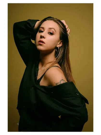 A moody and intense portrait with a dark, olive-green background. The lighting is focused on the model's face, creating a dramatic and captivating image.