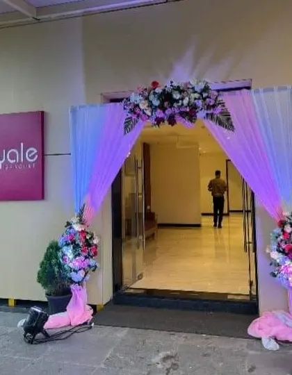 An entrance decorated with pink and purple drapery and floral bouquets, lit by spotlights.