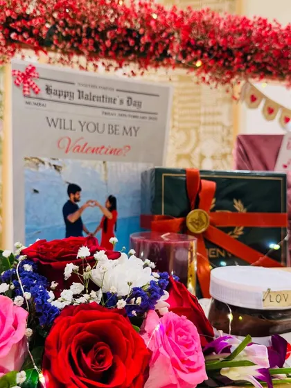 A close-up on the romantic details. The custom 'Will You Be My Valentine?' newspaper, fresh red roses, and a jar of Nutella labeled 'LOVE' come together to create a sweet and memorable moment.