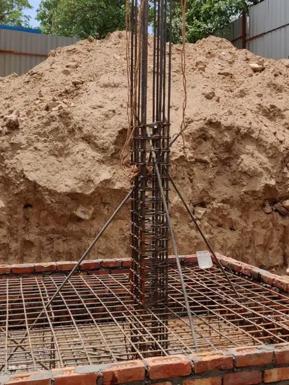 A close-up of a reinforced concrete column rising from the foundation, showing the dense network of steel bars that will give the building its strength.