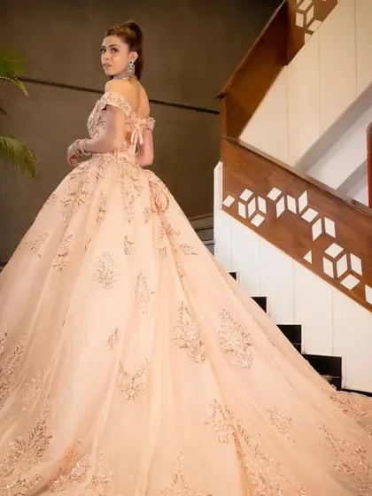 The back view of the peach ball gown, highlighting its long, flowing train and lace-up corset detail, ensuring a perfect fit.
