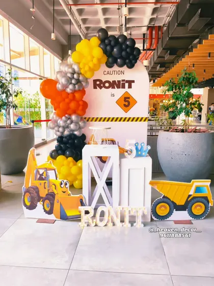 A fun and bright construction-themed 5th birthday party. This setup includes a custom "Caution" sign backdrop, character cutouts of a digger and dump truck, and a balloon garland in classic construction colors of yellow, black, and orange.