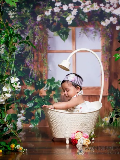 A quiet moment during a bath-themed shoot. The baby is sitting in a stylish tub surrounded by a lush, green floral backdrop, creating a serene and beautiful picture.