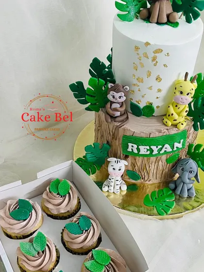 A wild jungle adventure on a two-tier cake. This design features adorable, handcrafted fondant animals like a monkey, giraffe, zebra, and elephant, with simple leaf-topped cupcakes.