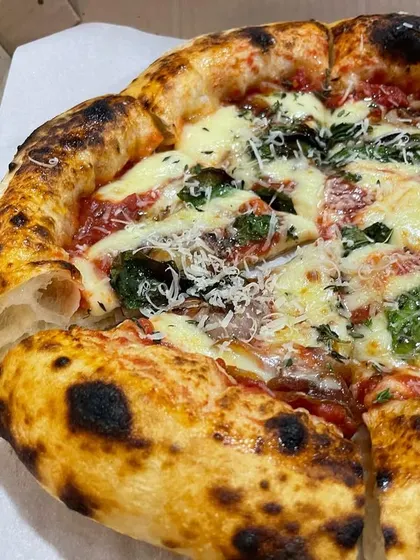 A beautiful pizza with a perfectly charred crust, topped with spinach and cheese. The slice is lifted to show the light and airy interior.