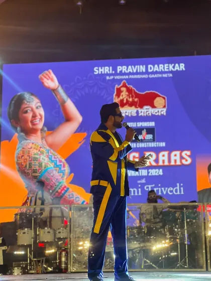 A wide shot of me hosting on the grand stage of Rangraas Navratri, with a huge LED screen featuring the event's branding and artists.