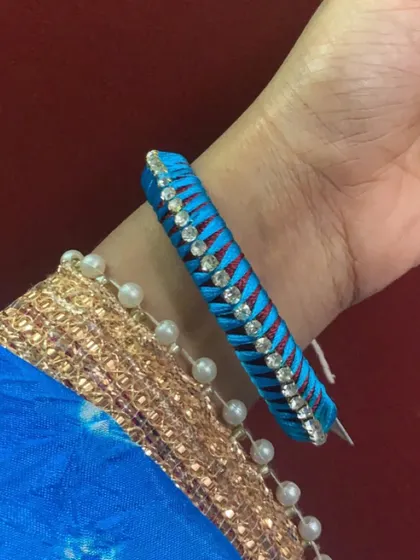 This single bangle features a beautiful criss-cross pattern in blue and red silk thread, with a line of sparkling stones.
