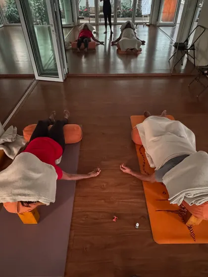 A moment of connection and restoration. Two students rest in a supported side-lying pose, showing how yoga can be a shared, loving practice.