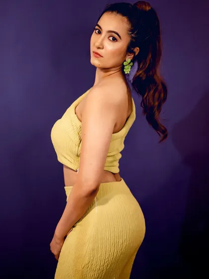A modern, coordinated yellow two-piece outfit. The side profile and confident pose against a solid purple background make the colors pop.