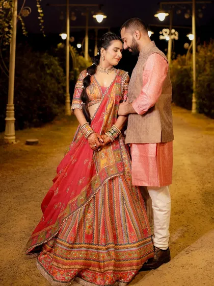 A full-length portrait of the couple on a lamp-lit path at night. The warm lighting and their gentle hold create a romantic, storybook atmosphere.