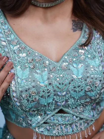 A close-up of the blouse on the ruffled blue lehenga. The intricate floral-patterned beadwork in shades of blue and silver is simply stunning.