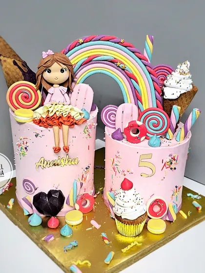 Welcome to Candyland. This vibrant pink cake duo is a sweet dream come true, decorated with lollipops, macarons, ice cream cones, and a custom doll topper made to look just like the birthday girl.