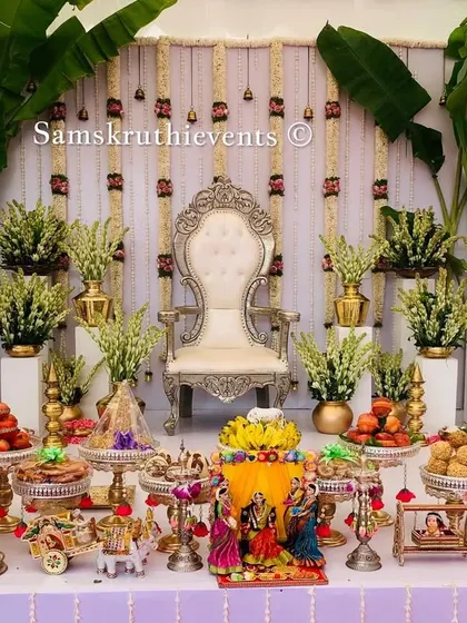 A closer view of the elegant white and gold themed Seemantha setup. You can see the detail in the floral arrangements, the silver offering stands, and the traditional doll scene at the center.