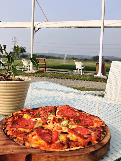 A delicious pepperoni pizza served at our outdoor seating area, with the lush driving range providing a beautiful, relaxing view.