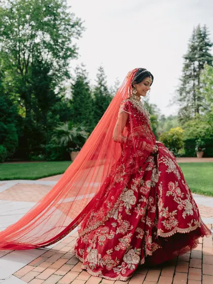 The side profile of this red lehenga highlights the delicate embroidery and the beautiful drape of the long veil, creating a truly cinematic bridal portrait.