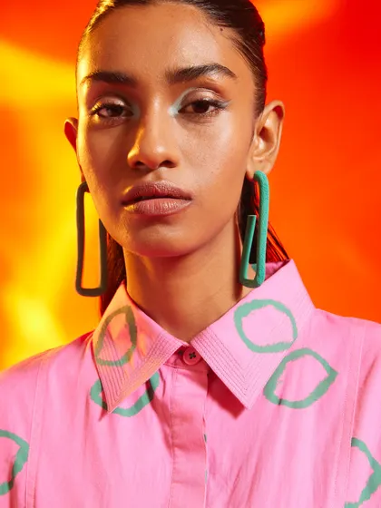 A close-up beauty shot from a campaign for Nakateki. The styling pairs a brightly colored shirt with oversized green earrings, creating a bold and playful color story.