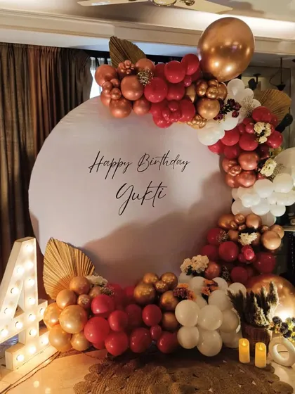 This is a beautiful birthday decoration I created for a celebration at home. It features a personalized circular backdrop with the birthday person's name, framed by a balloon arch in a sophisticated red, gold, and white color scheme. The illuminated '24' adds a special touch for a milestone birthday.