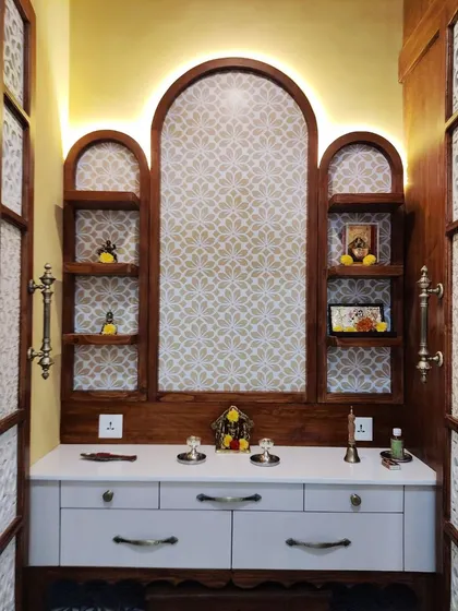 A wider view of the pooja room's interior, showing the white countertop with drawers for storage and the symmetrical arrangement of the display shelves.