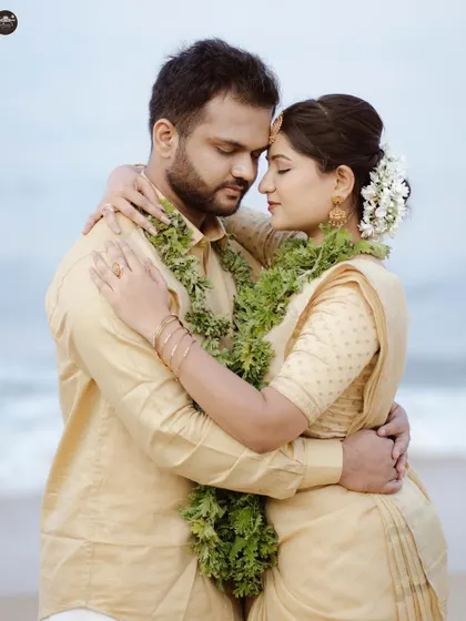 A close-up portrait of a couple embracing on the beach, both wearing traditional attire and leaf garlands. This image captures a tender, intimate connection against the backdrop of the sea.