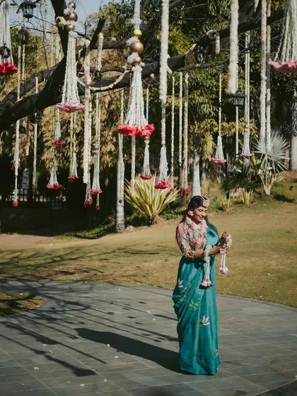 A serene portrait of the bride amidst the beautiful outdoor decor of her Haldi ceremony, holding a floral garland and taking in the moment.