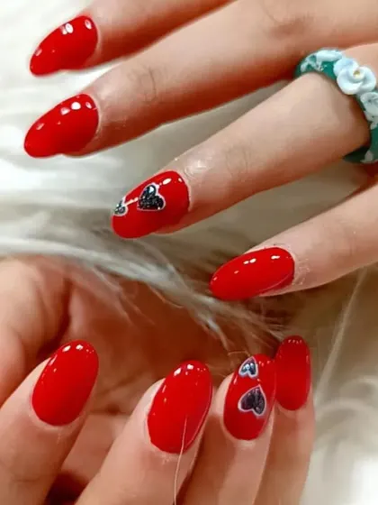 A vibrant red manicure gets a cute upgrade with tiny, shimmering heart decals on the accent nails.