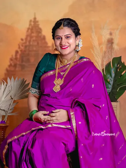 A smile that lights up the room. This happy mom-to-be is captured in our studio, looking radiant in a purple saree and traditional gold jewelry.