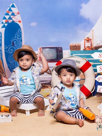 Twin boys ready for a day at sea in our nautical-themed photoshoot. Dressed in matching outfits, they are surrounded by beach props like surfboards, a toy boat, and starfish.