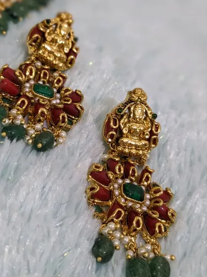 A close-up of the Lakshmi earrings with red coral and green bead drops.