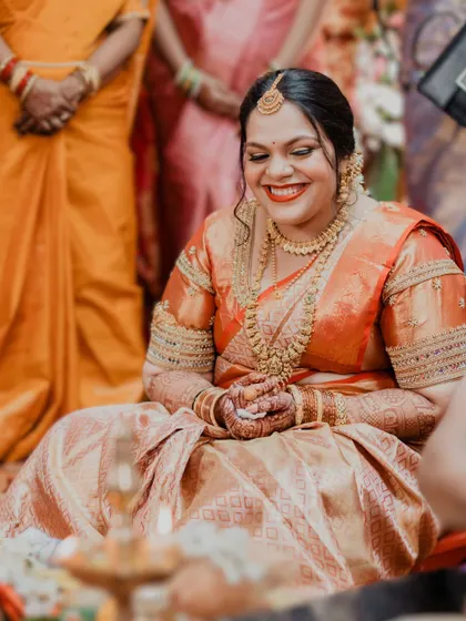 A candid shot of a happy South Indian bride during her wedding ceremony. Her makeup is bright and radiant, with a classic red lip that symbolizes joy and celebration.