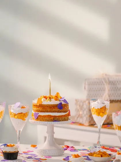 A beautifully styled birthday cake with a single lit candle, surrounded by confetti and desserts. This shot captures the quiet, celebratory mood of a personal milestone.