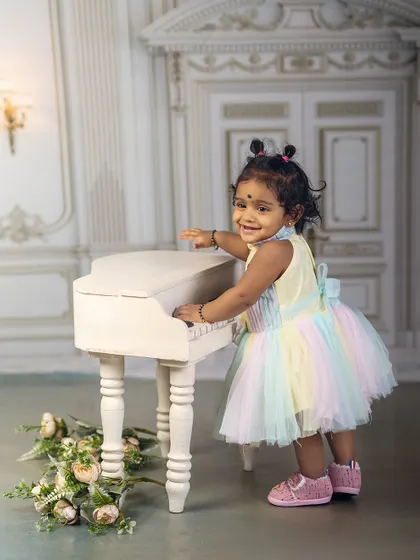 Her laughter is the sweetest song. This little girl in a rainbow dress creates her own music at the miniature piano, a perfect picture of joyful innocence.