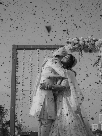 A dramatic black and white shot of the couple's Varmala kiss, with flower petals frozen in mid-air.
