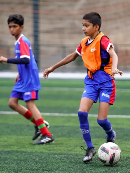 A player in an orange bib stays goal-side of his opponent. Our training covers crucial defensive principles like positioning and marking.