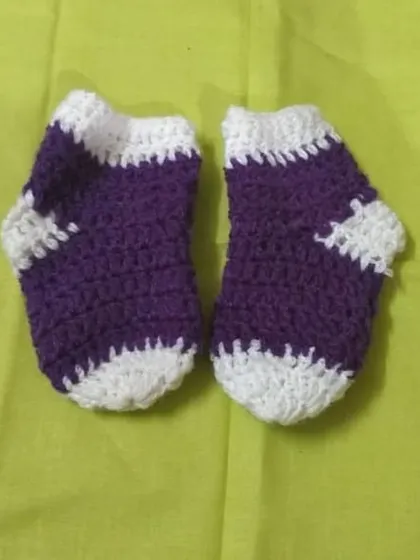 A pair of hand-knitted baby socks in purple and white, designed to be soft and warm.