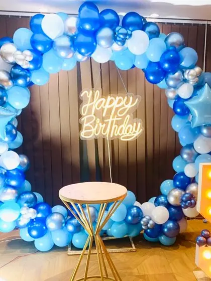A simple and modern birthday photo booth. The circular balloon arch in shades of blue and silver is paired with a "Happy Birthday" neon sign and a marquee number '5'.