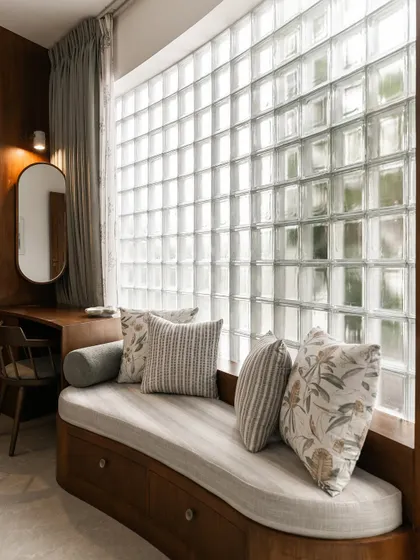 A curved bay window seat is set against a wall of glass blocks, a feature we love for the way it filters light. This detail provides privacy while bathing the space in a soft, diffused glow, creating a perfect reading nook.
