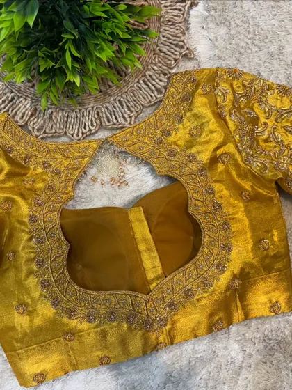 The back of the mustard yellow blouse, featuring a large, gracefully curved cut-out bordered by heavy gold embroidery.