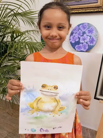 This young artist smiles as she shows off her beautifully rendered watercolor frog, complete with subtle color blending.