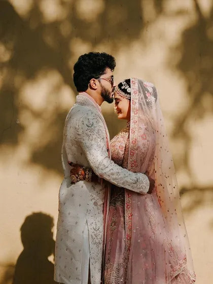 A silhouette of love. The groom gently kisses his bride's forehead against a sunlit wall, creating a timeless and artistic portrait.