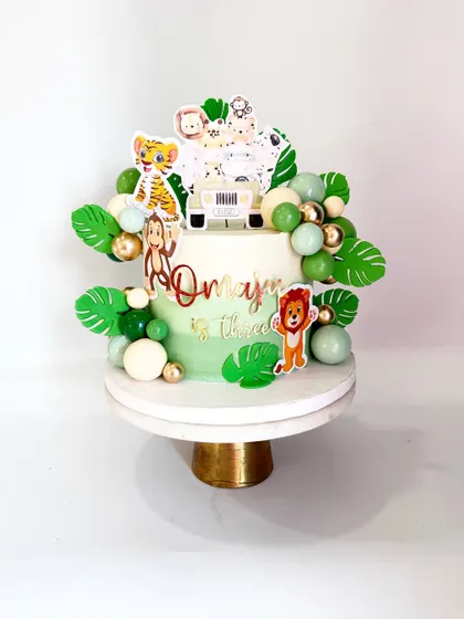A unique take on a jungle theme cake, using printed toppers instead of 3D figurines. This design is modern and fresh, with lush green leaves and a fun safari jeep.