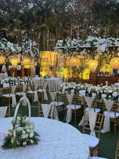 A wide view of an elegant outdoor engagement party, showcasing a mix of round and long table seating arrangements amidst lush greenery.
