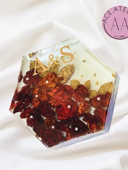 A hexagonal resin block preserving red and gold wedding flowers. The couple's initials, 'A & S', are featured in gold, creating a modern and personal keepsake to display on a desk or shelf.