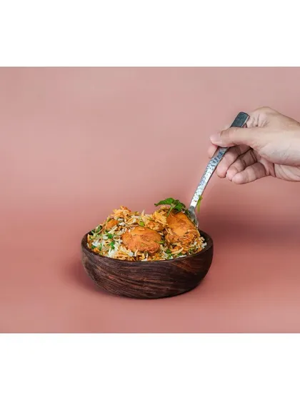 A wider shot of the chicken biryani, showing a hand with a spoon. This gives a better sense of scale and makes the dish feel ready to be eaten.